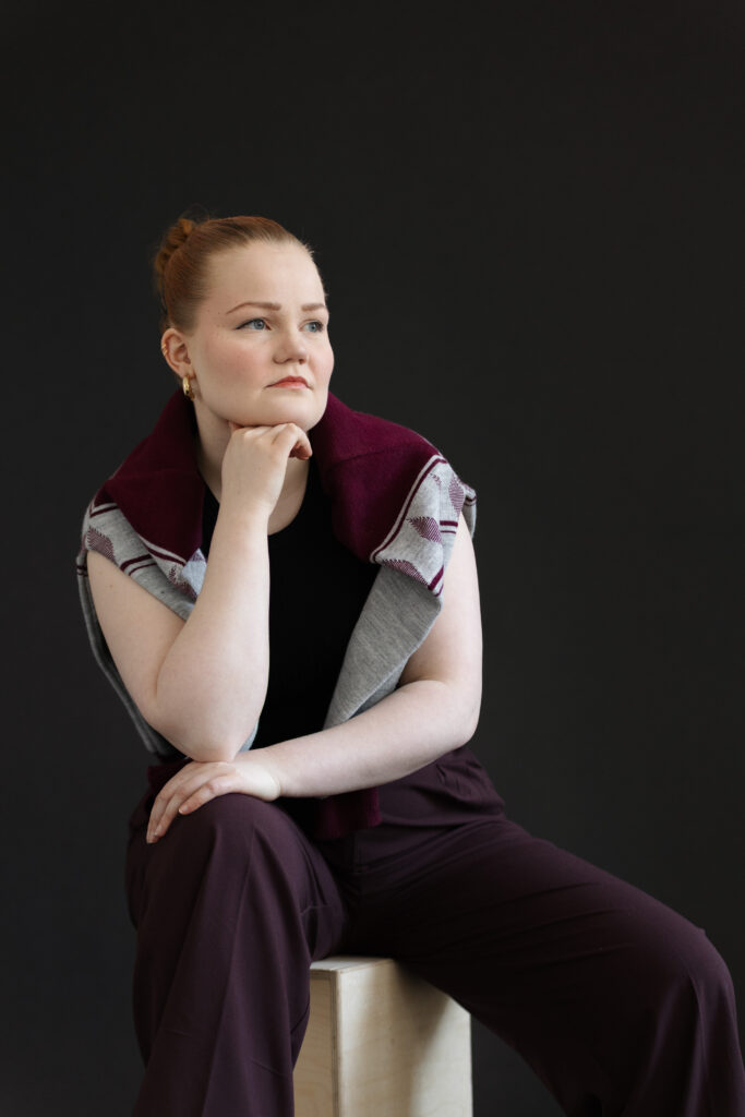 Kasketan yrittäjä ja toimitusjohtaja istuu mustan taustan edessä puisella laatikolla, käsi leuan alla. Yrittäjällä on harteillaan jussipaita. Ilme on vakava ja katse kohdistettuna kaukaisuuteen. 